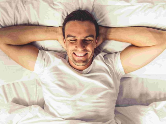 Uśmiechnięty mężczyzna leżący w łóżku - zdrowy sen