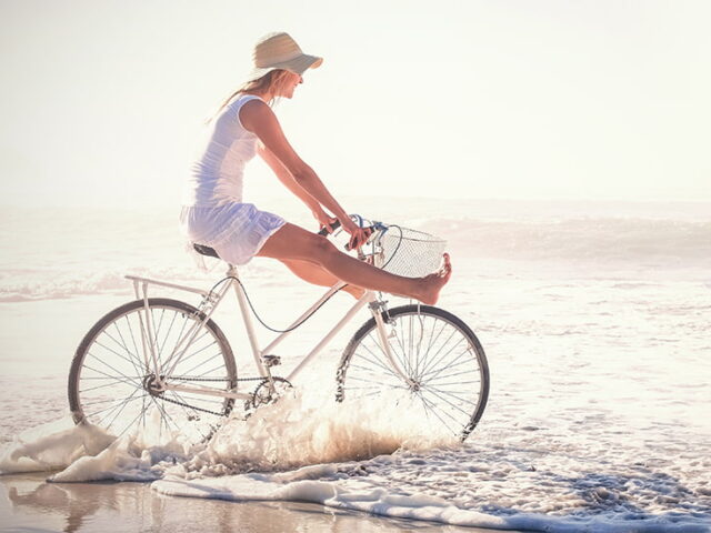 Kobieta wjeżdżająca rowerem do morza - zdrowe i piękne nogi na lato